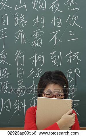 Stock Photograph - student hiding behind notepad in front of chinese characters written on chalk board. Fotosearch