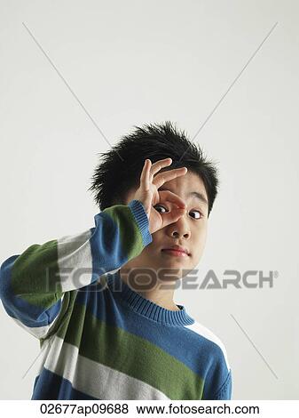 young boy making a O sign with fingers against his eye View Large Photo Image Stock Photo - young boy making a O sign with fingers against his eye. Fotosearch