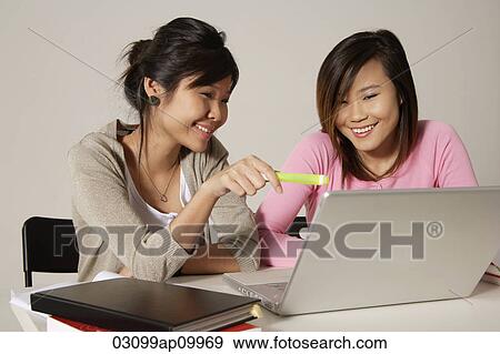 Two women sitting at desk and using a laptop. View Large Photo Image Stock Photo - Two women sitting at desk and using a laptop.. Fotosearch