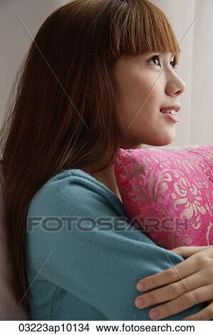 Picture - Asian girl holding pink pillow, looking up. Fotosearch