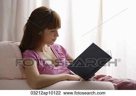 Stock Image - Asian girl reading book by window. Fotosearch