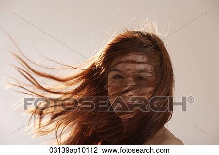 Stock Image - Young Asian girl with hair blowing in the wind.. Fotosearch