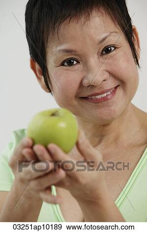 Mature Chinese woman holding green apple and smiling View Large Photo Image Stock Photo - Mature Chinese woman holding green apple and smiling. Fotosearch