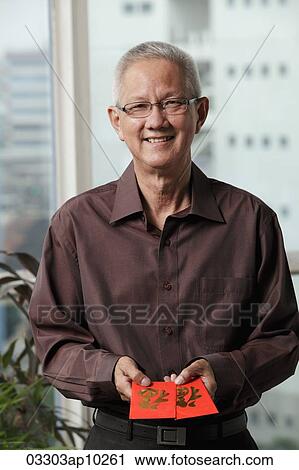 Stock Image - mature man holding red envelopes "hong bao". Fotosearch