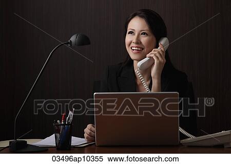 Chinese woman sitting at desk talking on phone and smiling View Large Photo Image Stock Photography - Chinese woman sitting at desk talking on phone and smiling. Fotosearch