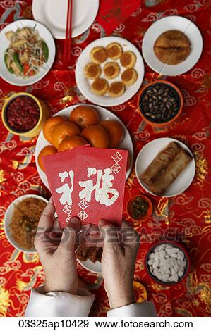 Hands holding red envelopes (Hong Bao) over table with Chinese food. View Large Photo Image Stock Photo - Hands holding red envelopes (Hong Bao) over table with Chinese food.. Fotosearch
