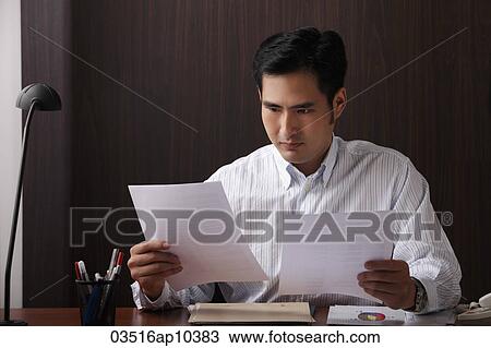 Man sitting at desk looking at paper View Large Photo Image Stock Image - Man sitting at desk looking at paper. Fotosearch