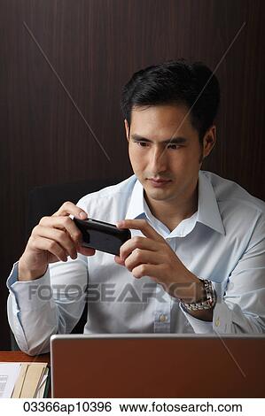 man sitting at desk looking phone View Large Photo Image Stock Photograph - man sitting at desk looking phone. Fotosearch