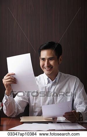 Man sitting at desk smiling at paper View Large Photo Image Picture - Man sitting at desk smiling at paper. Fotosearch