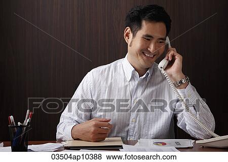 man sitting at desk talking on phone View Large Photo Image Stock Photo - man sitting at desk talking on phone. Fotosearch