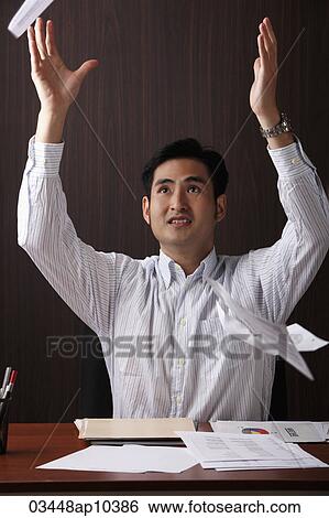 man sitting at desk throwing paper in the air View Large Photo Image Stock Photograph - man sitting at desk throwing paper in the air. Fotosearch