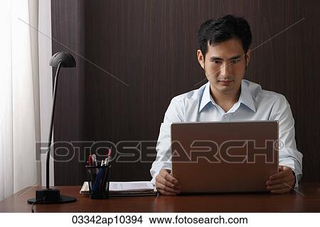 man sitting at desk working on laptop View Large Photo Image Picture - man sitting at desk working on laptop. Fotosearch