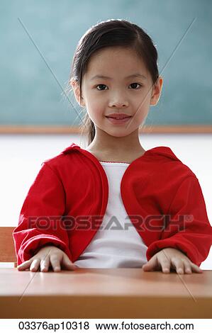 Stock Photo - Portrait of young girl sitting at desk in classroom. Fotosearch