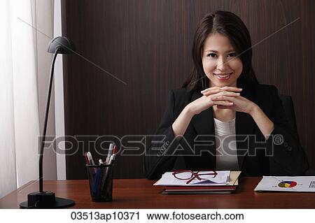 Stock Image - woman sitting at desk with folded hands smiling. Fotosearch