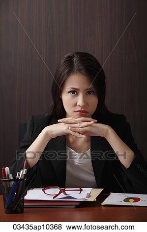 Stock Photo - Woman sitting at desk with head on hands frowning. Fotosearch