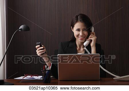 Woman sitting at her desk smiling and holding her phones View Large Photo Image Stock Photography - Woman sitting at her desk smiling and holding her phones. Fotosearch