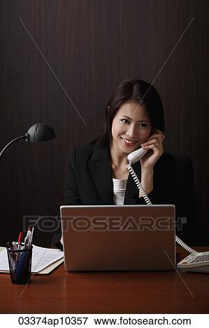 Woman sitting at her desk talking on phone View Large Photo Image Stock Photo - Woman sitting at her desk talking on phone. Fotosearch