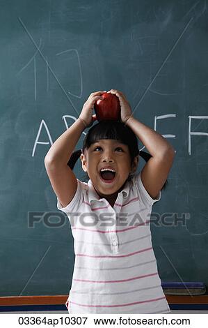 Stock Photo - young girl holding apple on top of her head and laughing. Fotosearch