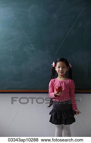 Stock Photo - Young girl holding red apple in front of chalk board. Fotosearch
