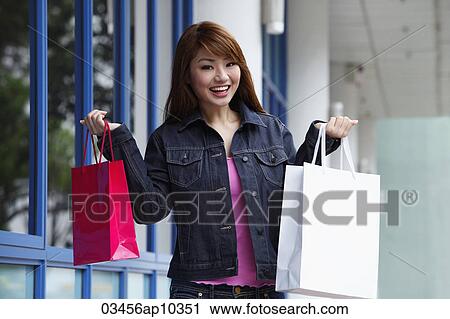 Stock Image - Young woman holding up shopping bags and smiling. Fotosearch
