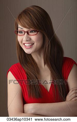 Stock Image - Young woman in red dress wearing red sunglasses looking away and smiling. Fotosearch