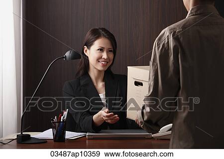 Young woman sitting at desk accepting a delivery View Large Photo Image Stock Photo - Young woman sitting at desk accepting a delivery. Fotosearch