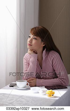 Young woman sitting at table looking our window View Large Photo Image Stock Photo - Young woman sitting at table looking our window. Fotosearch