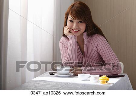 Young woman sitting at table near table with coffee. View Large Photo Image Stock Photograph - Young woman sitting at table near table with coffee.. Fotosearch