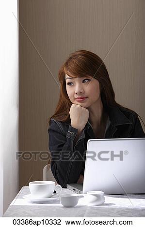Young woman sitting at table with laptop View Large Photo Image Stock Image - Young woman sitting at table with laptop. Fotosearch