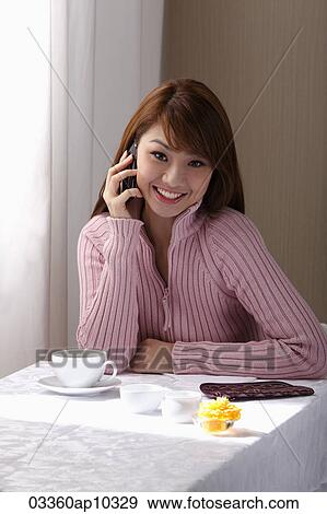 Young woman sitting at table with coffee and talking on phone View Large Photo Image Stock Photo - Young woman sitting at table with coffee and talking on phone. Fotosearch
