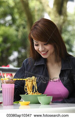 Young woman sitting outside eating noodles View Large Photo Image Stock Photo - Young woman sitting outside eating noodles. Fotosearch