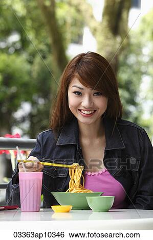 Young woman sitting outside eating noodles and smiling View Large Photo Image Stock Photograph - Young woman sitting outside eating noodles and smiling. Fotosearch