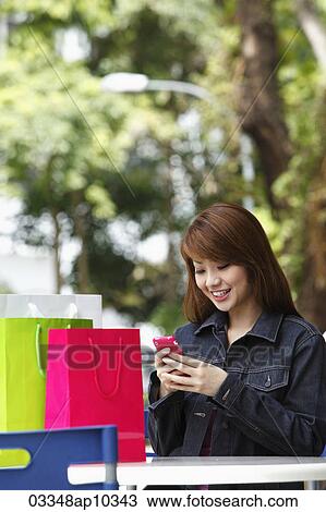Young woman sitting outside with shopping bags and looking at phone View Large Photo Image Stock Image - Young woman sitting outside with shopping bags and looking at phone. Fotosearch