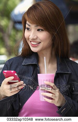Young woman smiling holding a phone and drink View Large Photo Image Stock Photo - Young woman smiling holding a phone and drink. Fotosearch
