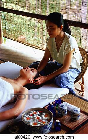 Stock Image - Asian masseuse massaging temples of Eurasian female lying down. Fotosearch
