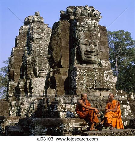 Stock Image - Cambodia, Angkor Thom, monks sitting at foot of Face towers, the Bayon. Fotosearch