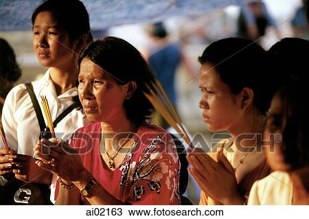Stock Image - Cambodia, Phnom Penh, Worshippers praying with incense at a temple.. Fotosearch