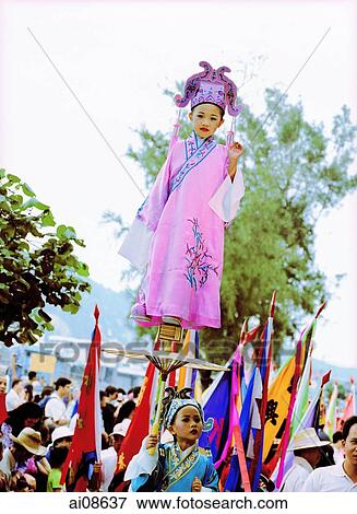 Stock Photo - China, Hong Kong, Cheung Chau Island, Girl wearing a traditional costume, standing on tiny foothold held up by young boy during the Bun Festival procession in 2000. Fotosearch