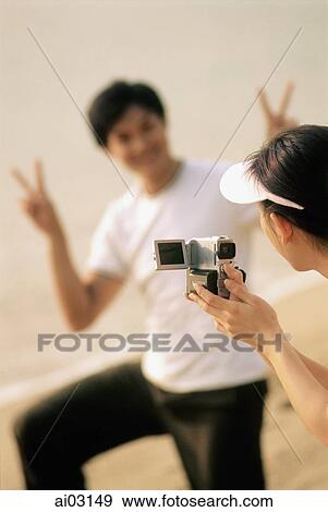 Couple at beach, woman filming man making peace sign View Large Photo Image Stock Photo - Couple at beach, woman filming man making peace sign. Fotosearch