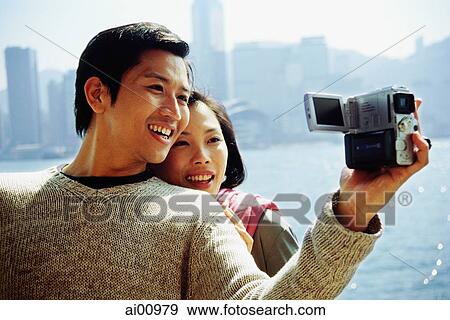 Couple by waterfront, man holding video camera View Large Photo Image Stock Photo - Couple by waterfront, man holding video camera. Fotosearch