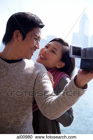 Couple looking at each other by waterfront, man holding video camera View Large Photo Image Stock Image - Couple looking at each other by waterfront, man holding video camera. Fotosearch