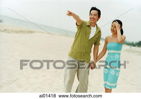Couple on beach holding hands, man pointing in distance ( high grain) View Large Photo Image Stock Photo - Couple on beach holding hands, man pointing in distance ( high grain). Fotosearch