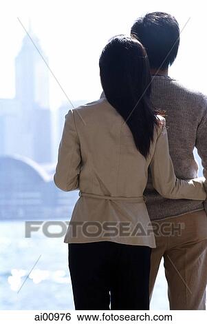 Couple standing by waterfront looking at Hong Kong skyline, rear view View Large Photo Image Stock Photograph - Couple standing by waterfront looking at Hong Kong skyline, rear view. Fotosearch