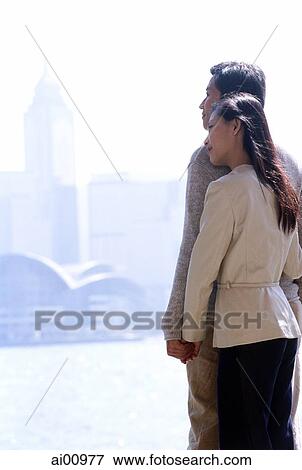 Couple standing by waterfront, with Hong Kong skyline View Large Photo Image Stock Photo - Couple standing by waterfront, with Hong Kong skyline. Fotosearch