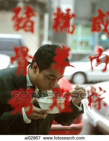 Stock Photo - Executive eating bowl of noodles, seen through glass window with Chinese characters.. Fotosearch