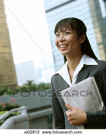 Stock Image - Executive woman holding newspaper, buildings in background.. Fotosearch