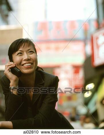 Stock Image - Executive woman on cellular phone, shops in background.. Fotosearch