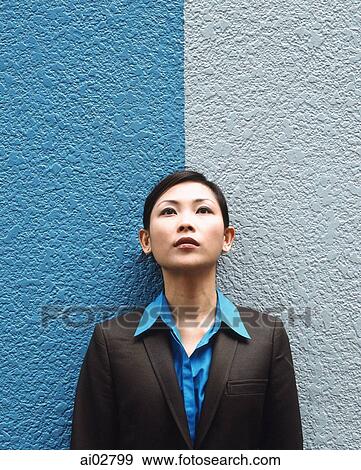 Stock Photo - Executive woman standing against split colored background, looking up.. Fotosearch