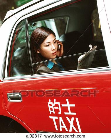 Stock Photo - Executive woman using cellular phone and reading newspaper in taxi.. Fotosearch