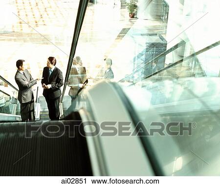 Stock Image - Executives on escalator talking.. Fotosearch